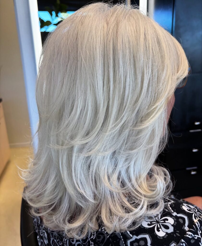A back view of a woman with a medium-length icy white layered haircut featuring tiered layers and flicked-out ends.