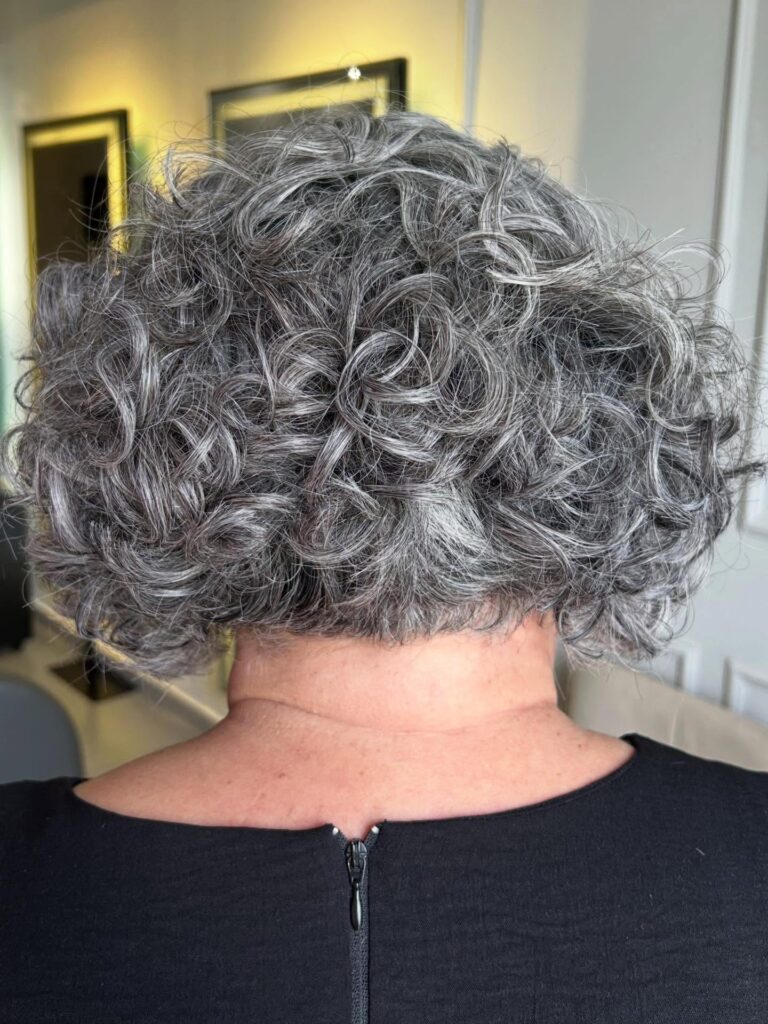A woman over 60 with a short curly salt-and-pepper bob that is tapered at the nape of the neck.