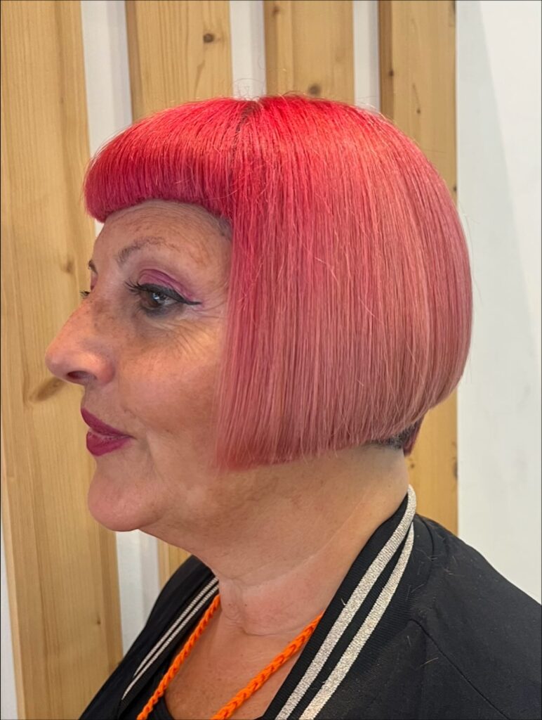 A side profile of a woman with a bright pink blunt bob and very short straight bangs.