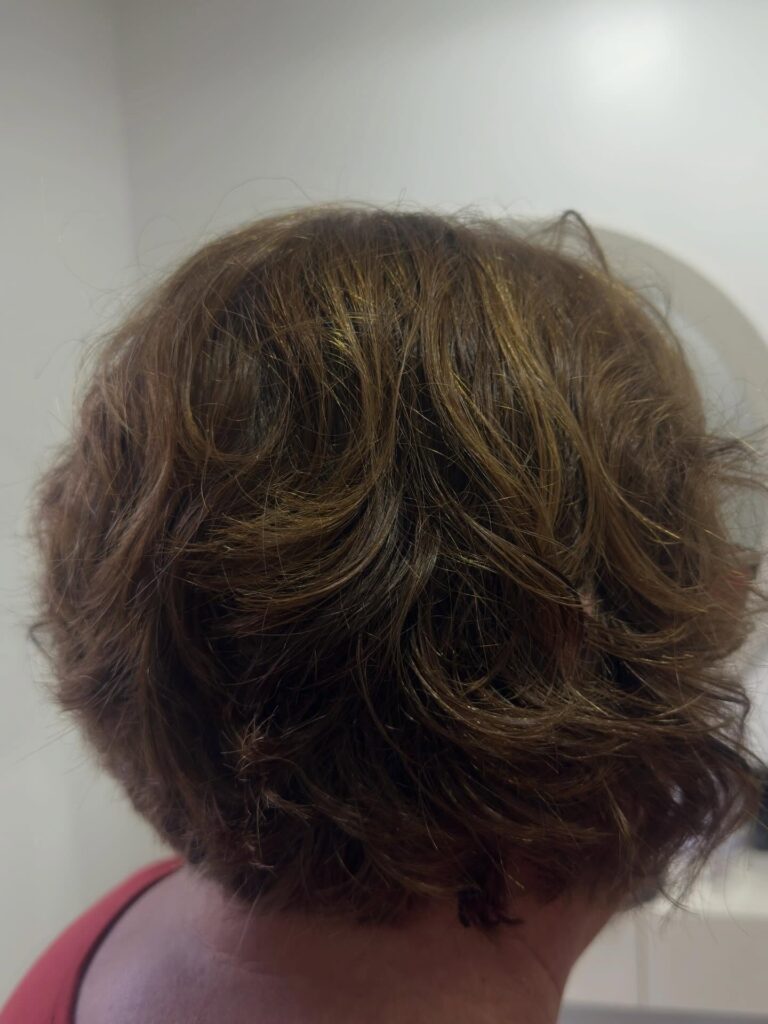 A back view of a woman with a wavy brunette bob featuring golden highlights and voluminous layers.