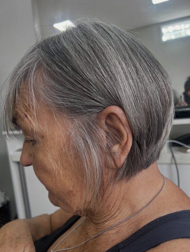 A woman over 60 with a straight silver-and-grey bob tucked behind her ear to show a clean nape.