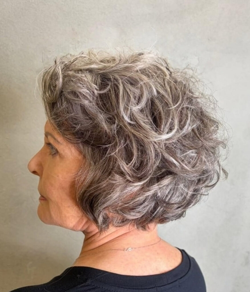 A side profile of a woman with a voluminous curly bob in a salt-and-pepper grey color.