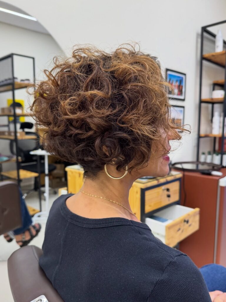 A woman over 60 with an inverted curly bob featuring chestnut hair and bright copper highlights.