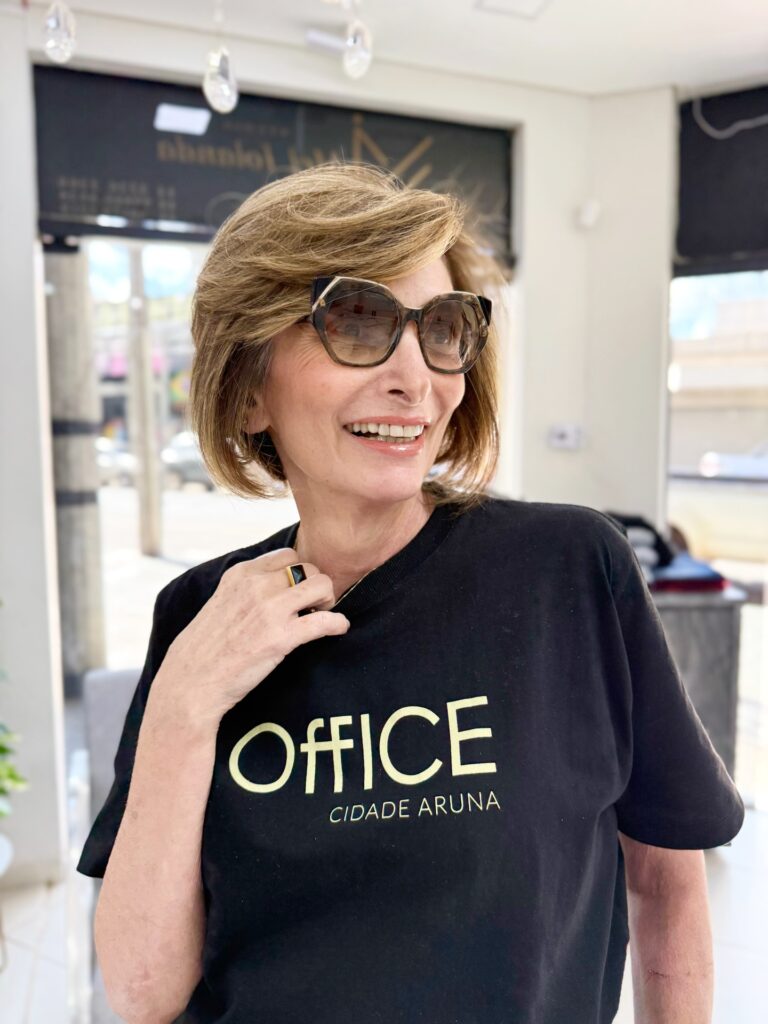 A smiling woman wearing a honey-brown short bob with voluminous side-swept layers and stylish sunglasses.