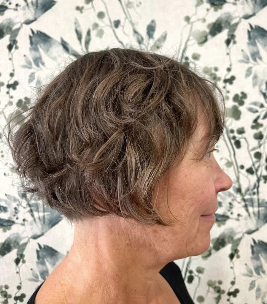 A side profile of a woman with an ash-brown mushroom bob featuring wispy layers and natural wavy texture.