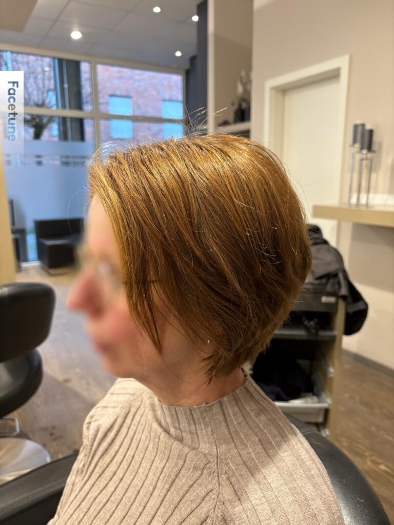 A woman over 60 with a short tapered bob in a bright copper-red shade featuring side-swept bangs.