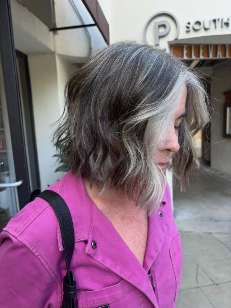 A woman with a neck-length wavy charcoal bob featuring a bold silver money piece in the front.