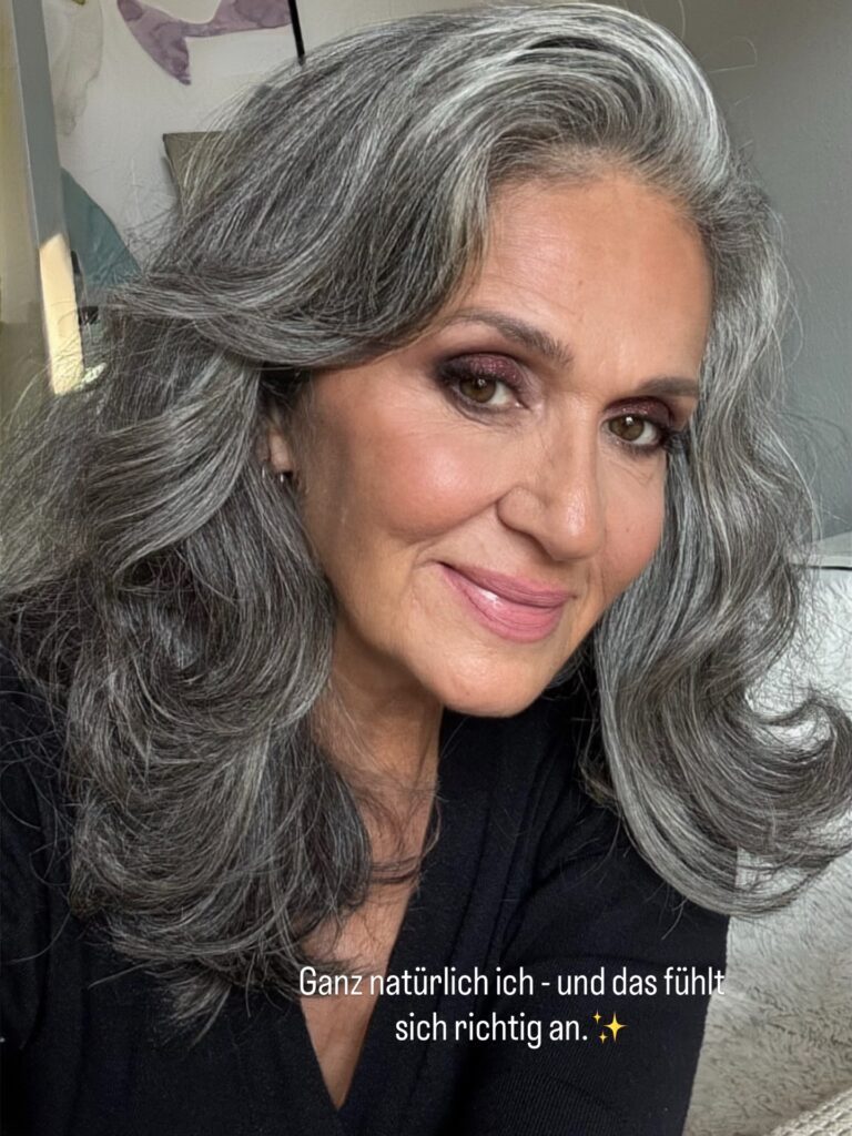 A woman with medium-length voluminous grey hair styled in large glamorous waves and a side sweep.