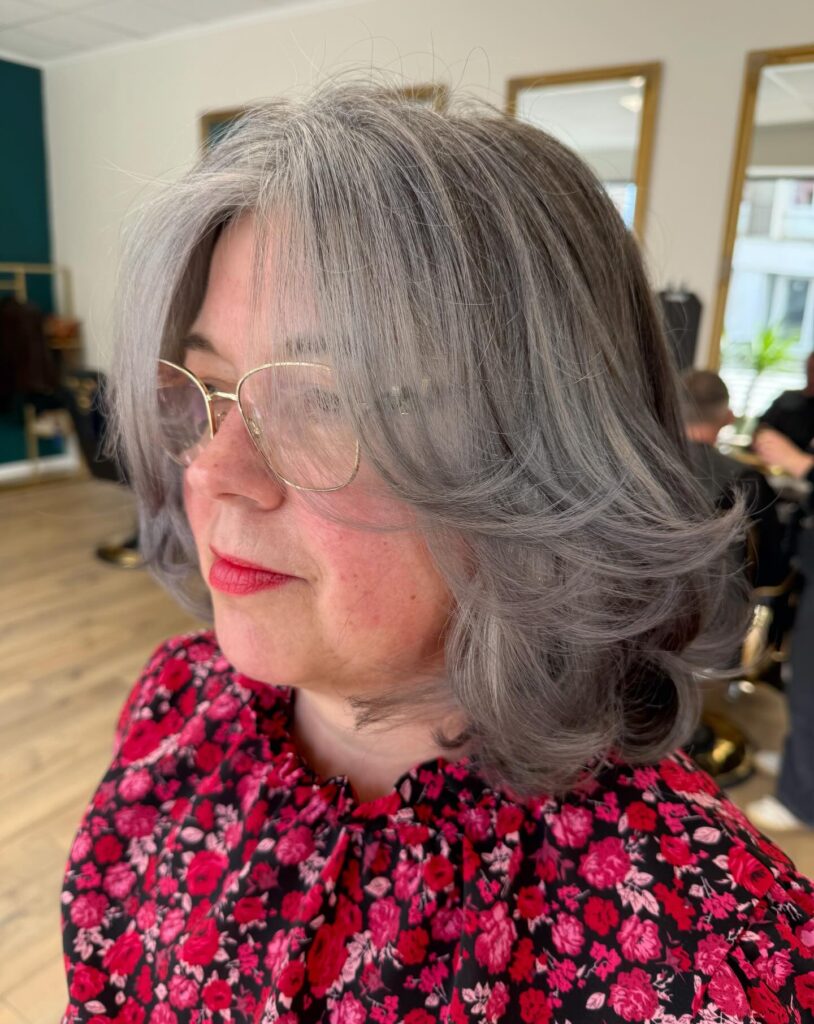 A woman with a medium-length steel-blue-and-silver bob featuring winged layers and wispy bangs.