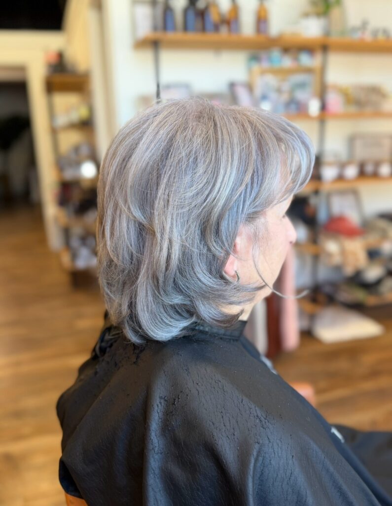 A side profile of a woman with a feathered medium-length silver haircut and wispy bangs.