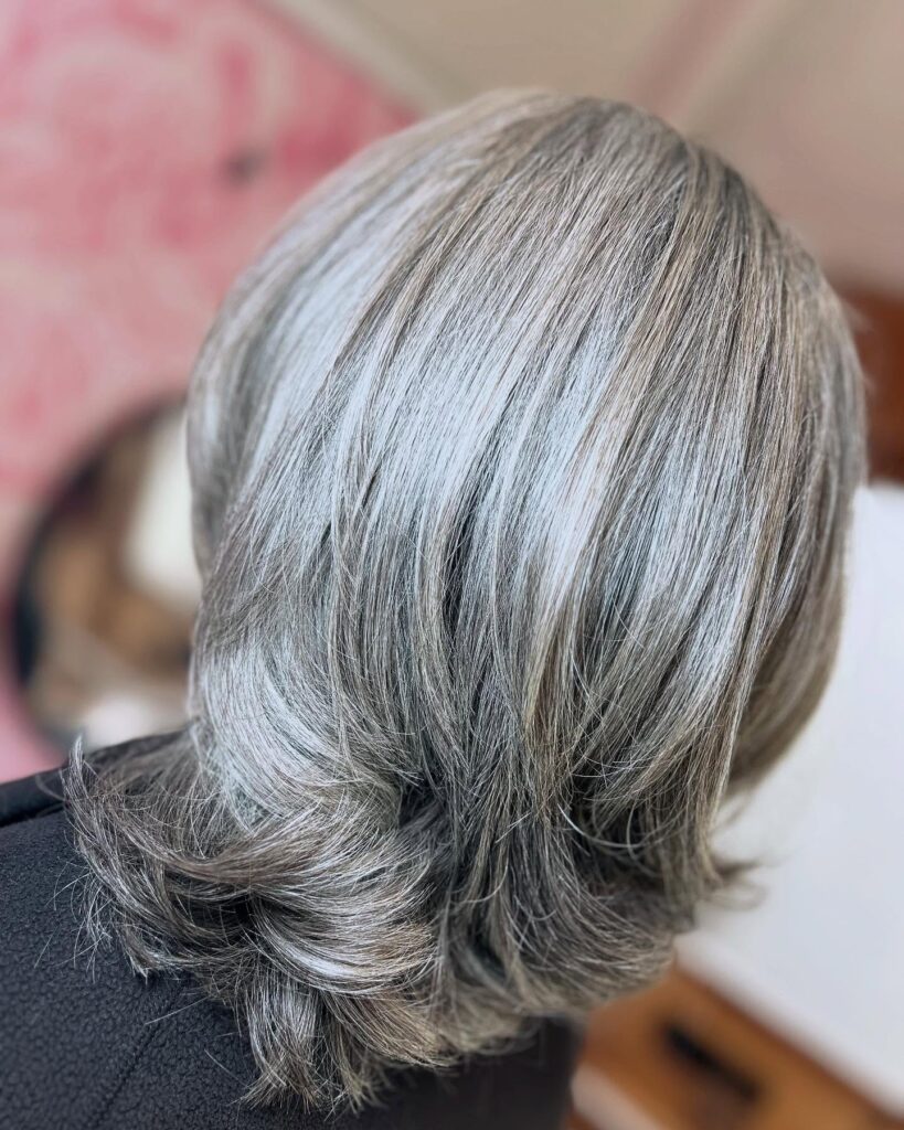A close-up back view of a woman with medium-length grey hair featuring layered ends flipped outward.