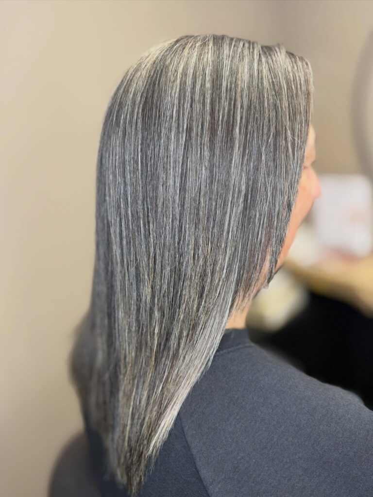 A side and back view of a woman with straight medium-length hair featuring high-contrast silver and charcoal highlights.