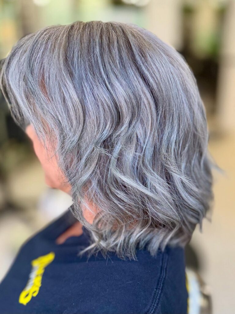 A close-up side view of a woman with a medium-length silver bob styled in soft textured waves.