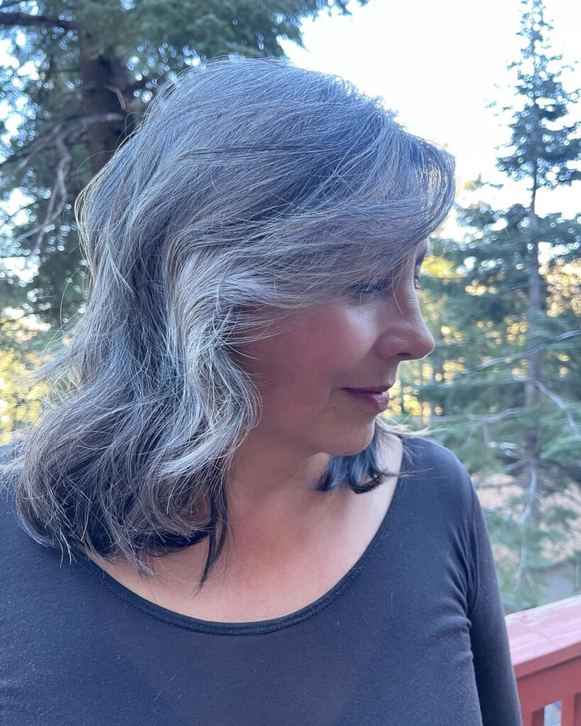A side profile of a woman with medium-length wavy salt and pepper hair in an outdoor setting.