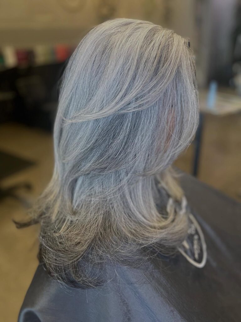 A side profile of a woman with medium-length silver hair featuring long cascading layers and soft flipped ends.