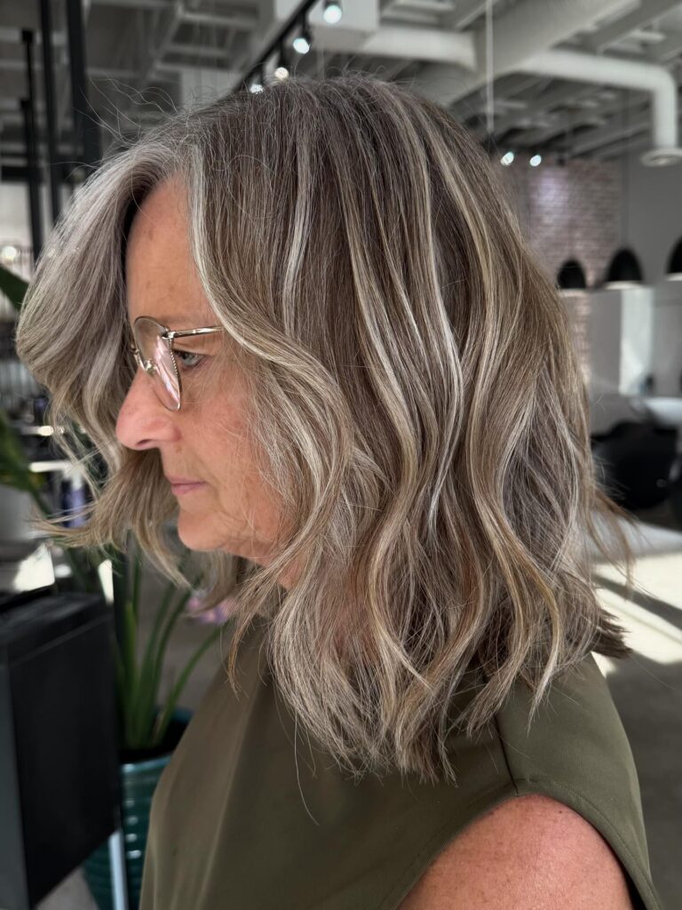 A woman with shoulder-length wavy hair featuring a blend of ash blonde and bright silver highlights.