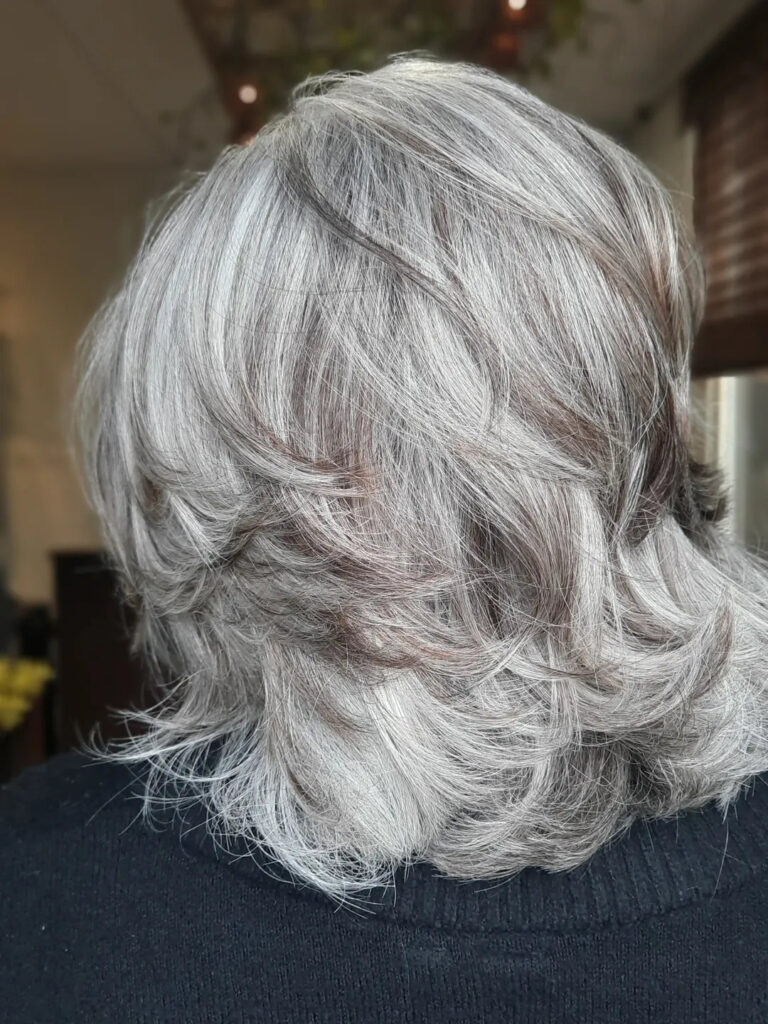 A back view of a woman with a textured medium-length ash-silver haircut featuring many feathered layers.