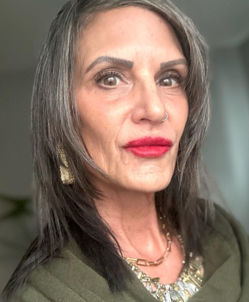 A woman with medium-length straight pewter grey hair featuring razor-cut layers and a side part.
