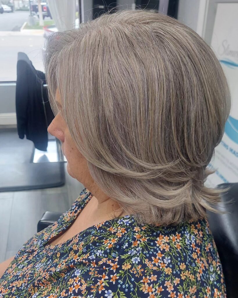 A side view of a woman with a medium-length mushroom-grey haircut featuring feathered layers and flicked ends.