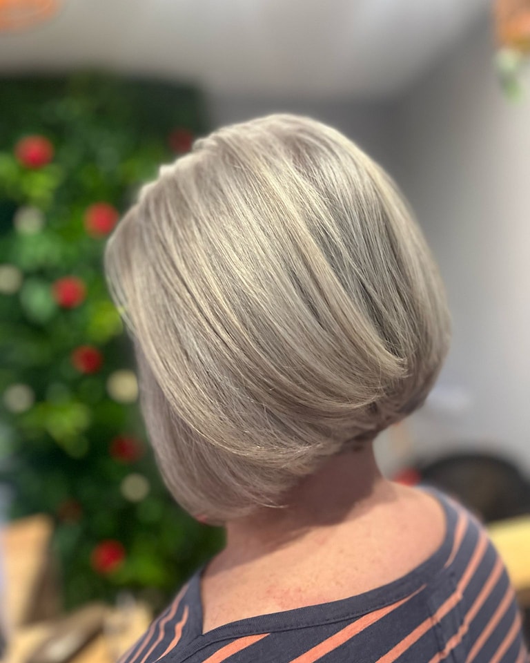 A woman with a medium-length angled bob hairstyle featuring stacked layers in the back and a blend of silver and ash blonde tones.