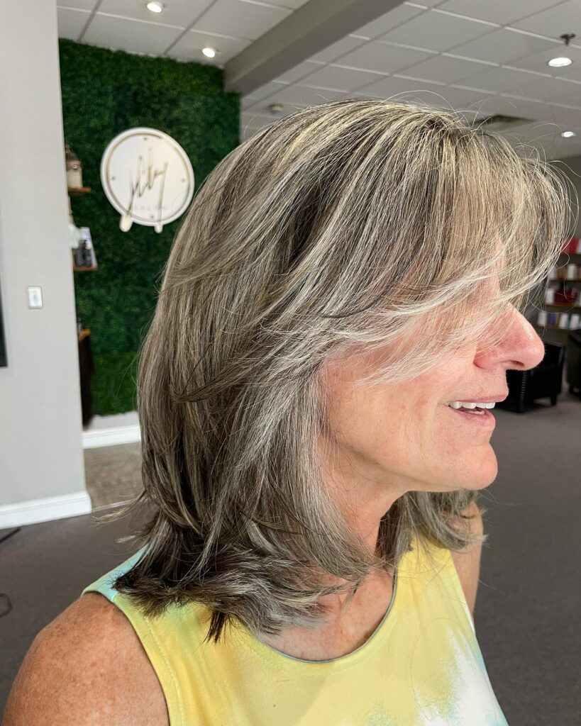 A woman in profile with a shaggy medium-length bob featuring ash-blonde highlights and long side-swept layers.