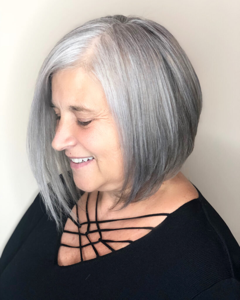 A woman with a sleek, asymmetrical medium bob in a bright natural silver-grey color with a deep side part.