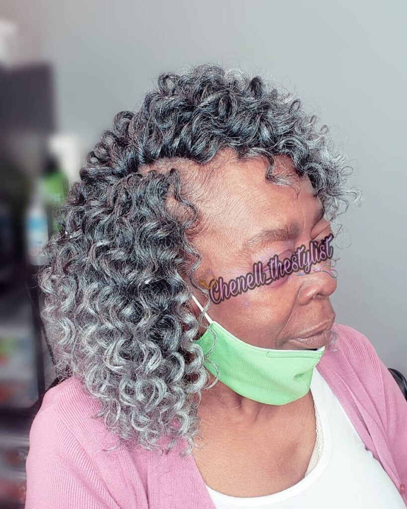A woman with a medium-length curly bob featuring tight salt-and-pepper ringlets and a side part.