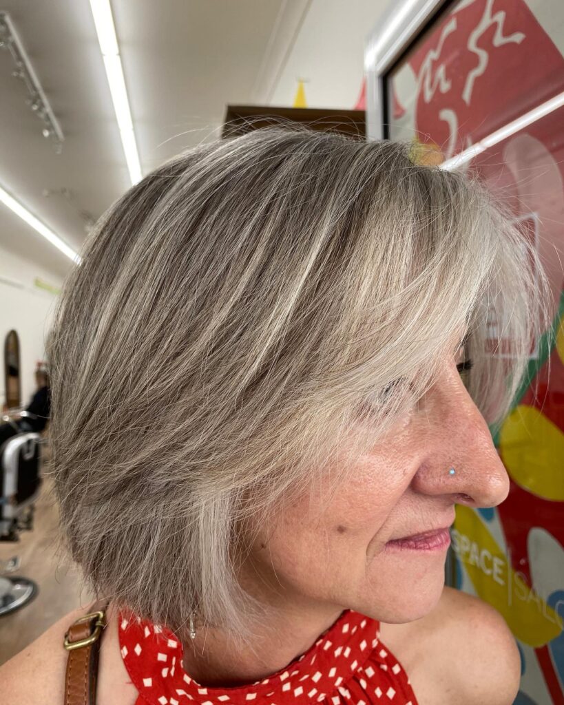 A woman over 60 with a layered ash-grey bob featuring feathered face-framing pieces and a soft side fringe.