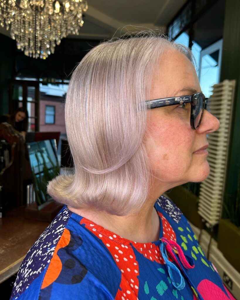 A woman over 60 with a sleek medium-length bob in an iridescent pearl and lilac shade with flipped-out ends.