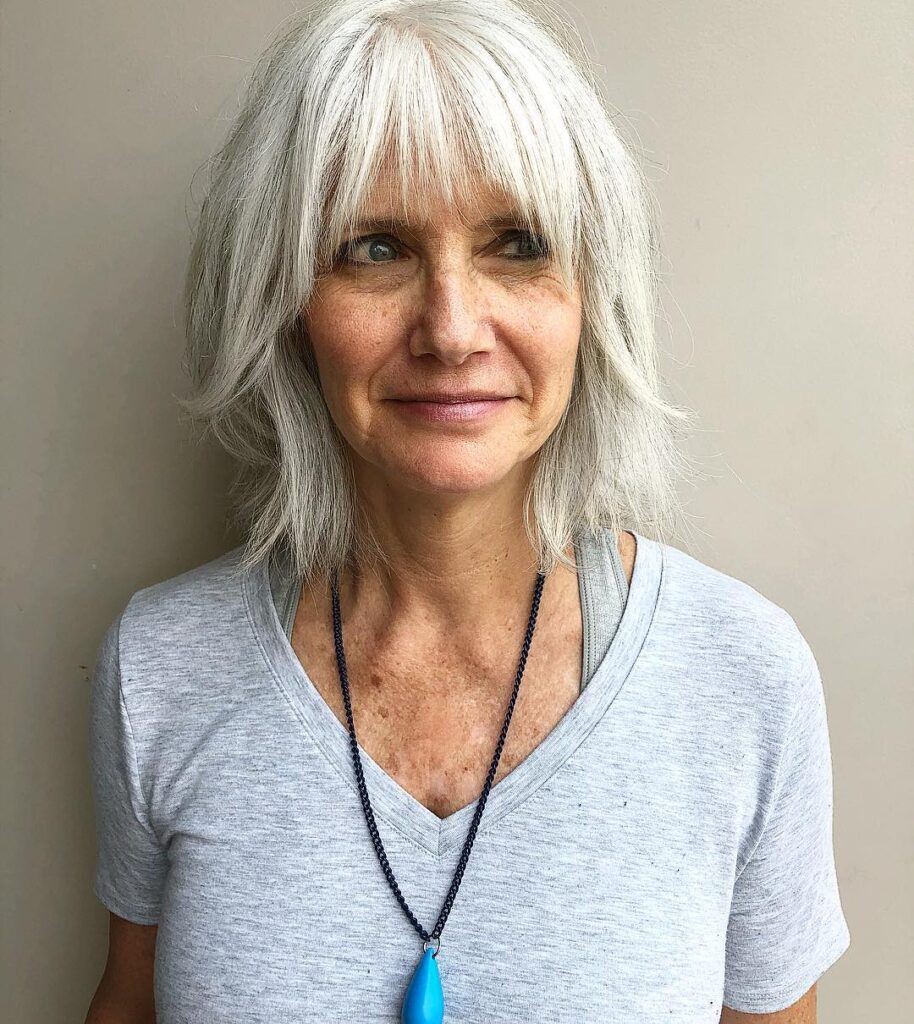 A woman with a medium-length shaggy silver bob featuring wispy bangs and textured layers.