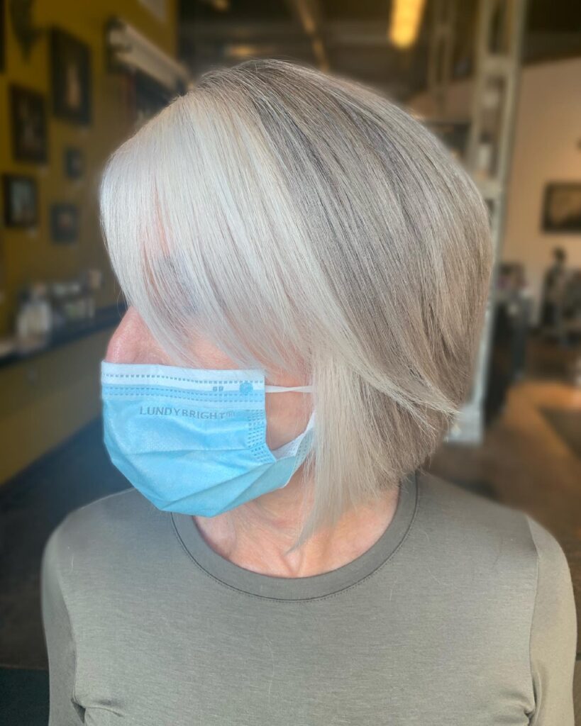 A woman with a straight medium bob in an ashy taupe shade featuring a thick bright silver highlight at the front.