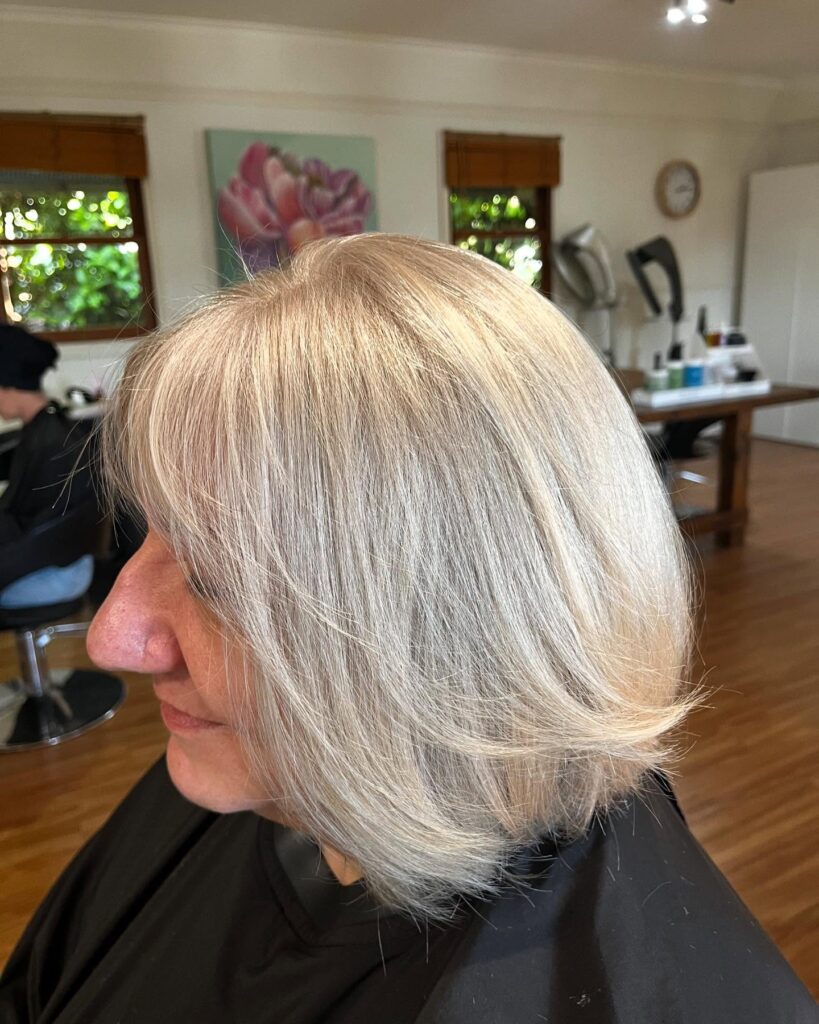 A woman with a medium-length, pearl blonde bob featuring a wispy fringe and soft layered ends.