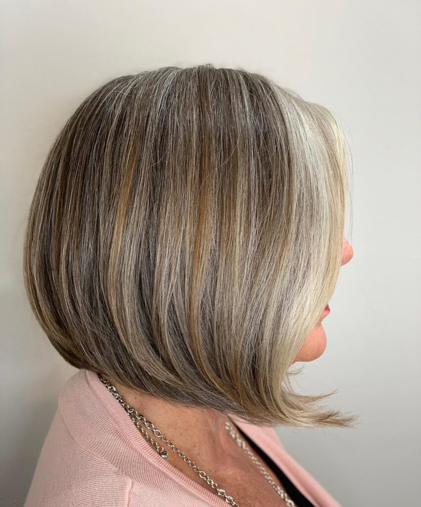 A woman over 60 showcasing a sleek inverted bob with a blend of salt and pepper tones and light blonde highlights.