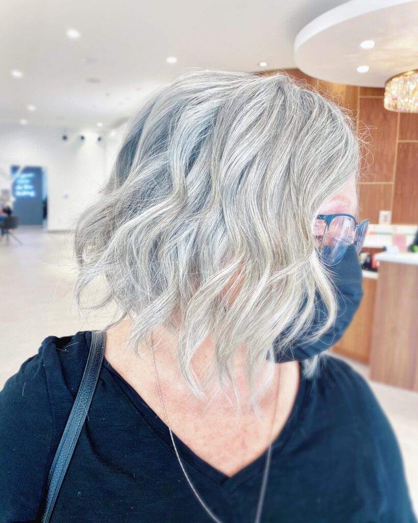 A woman wearing glasses with a medium-length silver bob styled in loose beachy waves.