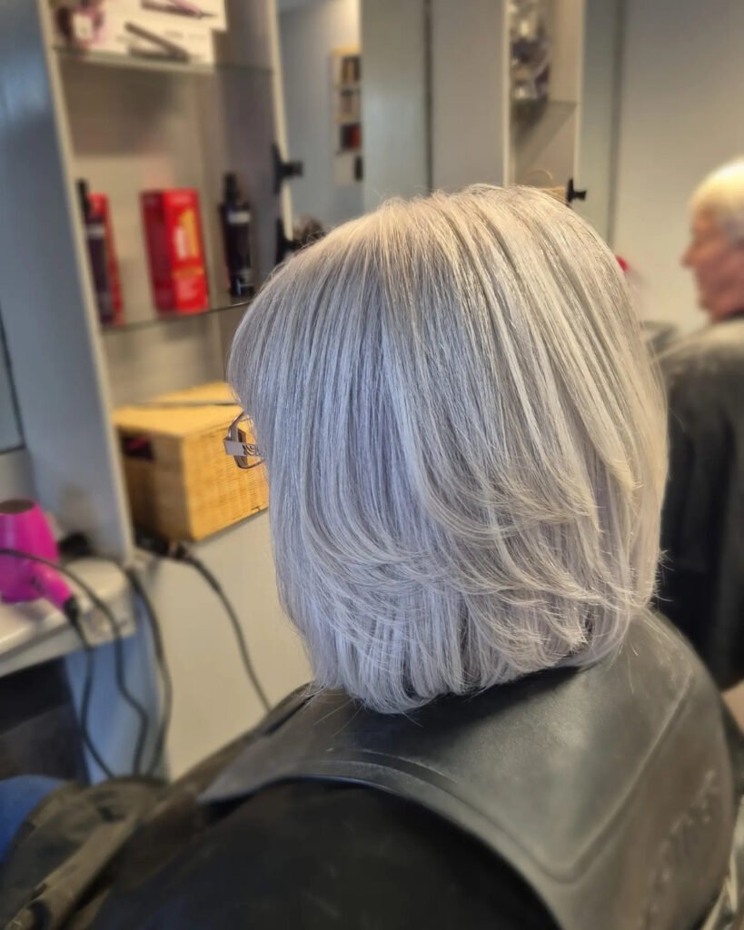 A woman over 60 with a rounded ash blonde bob featuring soft inward-curving layers and a sleek finish.