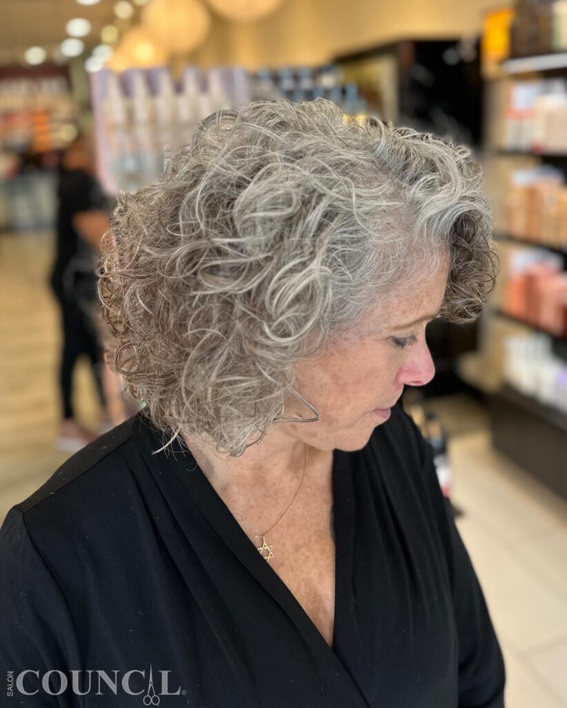 A woman in profile with a medium-length curly bob in a natural silver and charcoal grey blend.