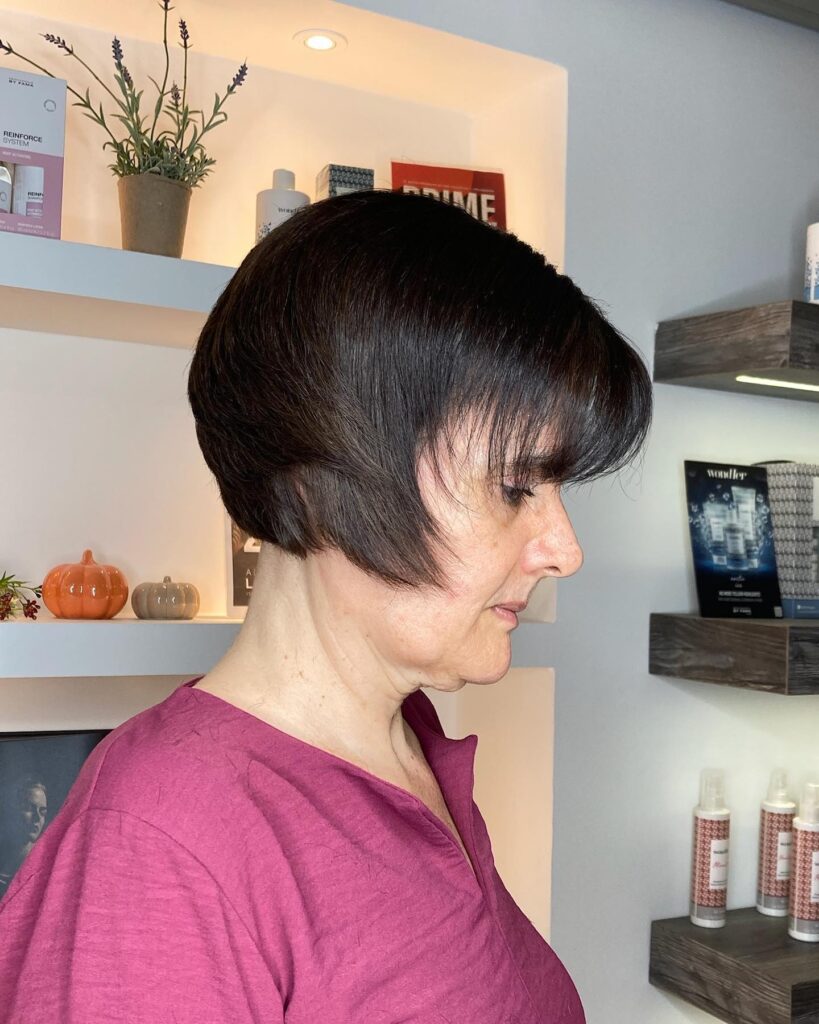 A side profile of a woman with a dark brunette long pixie cut featuring a rounded back and angled side sections.