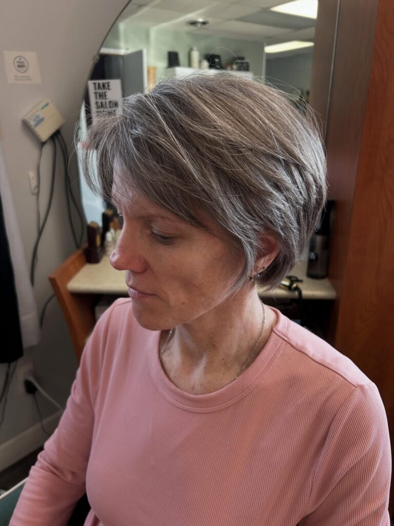 A woman with an ash-grey bixie haircut featuring long flowing layers and a soft side-swept fringe.