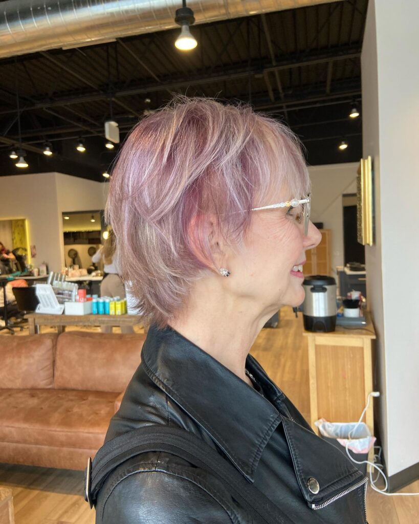 A woman over 60 with a layered pastel lavender pixie bob featuring feathery texture and wispy bangs.