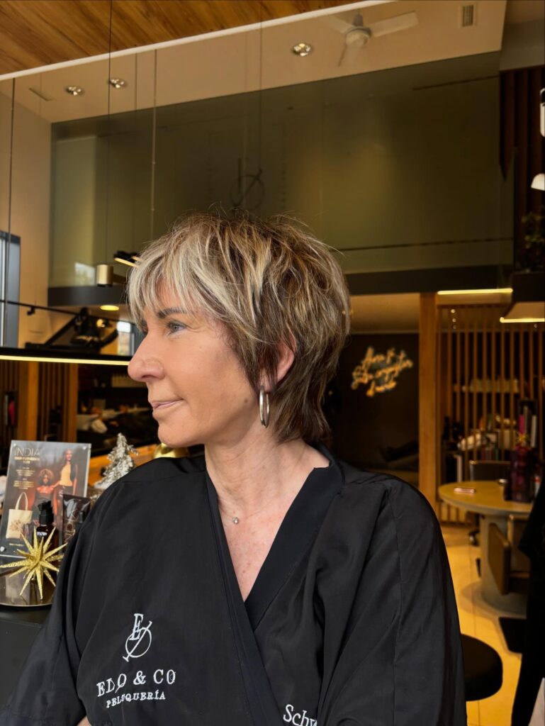 A woman with a shaggy caramel bixie haircut featuring choppy layers and bright blonde face-framing highlights.
