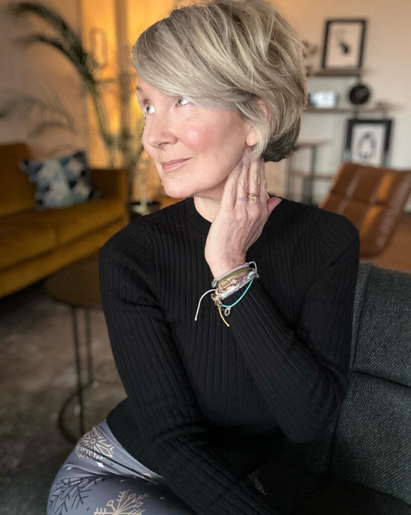 A woman with an elegant side-swept ash blonde bixie cut featuring voluminous layers and a deep side part.