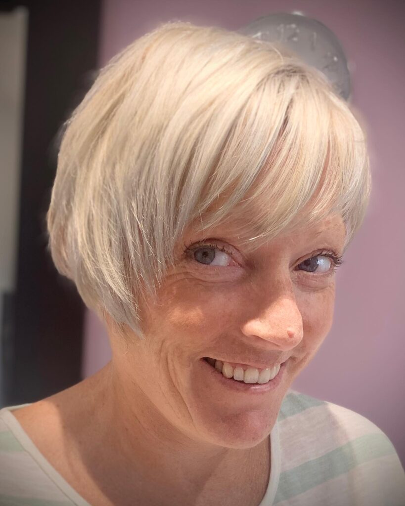 A smiling woman with a wispy platinum blonde pixie bob and a soft side-swept fringe.