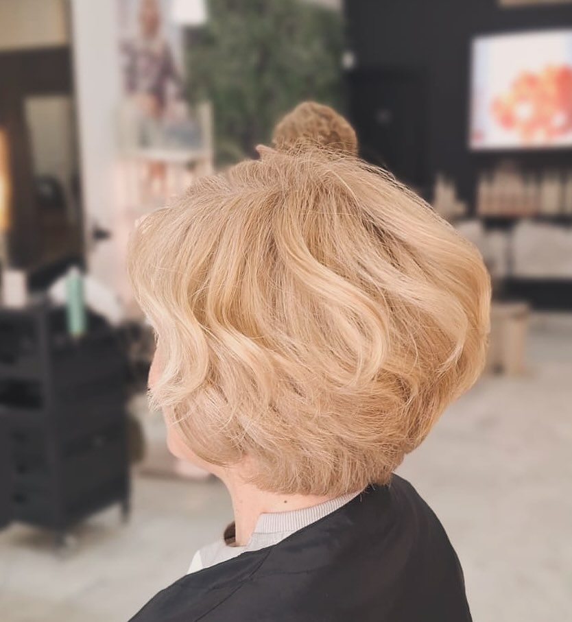 A woman over 60 with a soft, champagne-blonde pixie bob styled in romantic waves with voluminous texture.