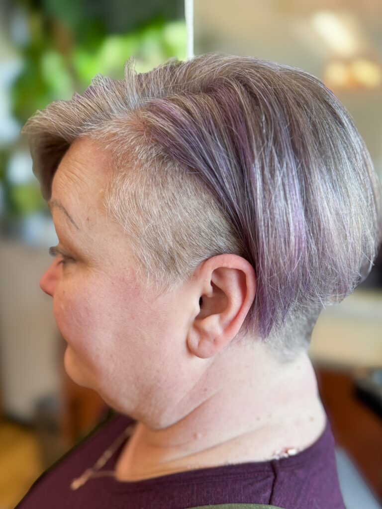 A side profile of a woman with a silver and lilac pixie bob featuring a bold shaved undercut.