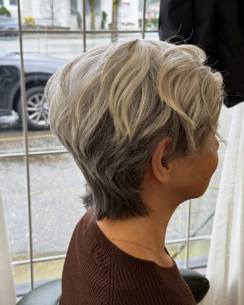 A side profile of a woman with a textured champagne silver bixie cut featuring dark grey lowlights at the nape.