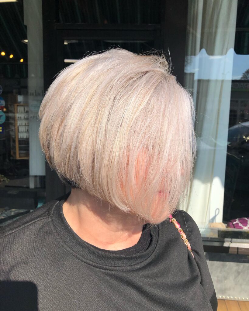 A side view of a woman with a sleek, creamy pearl blonde pixie bob featuring a voluminous graduated back.