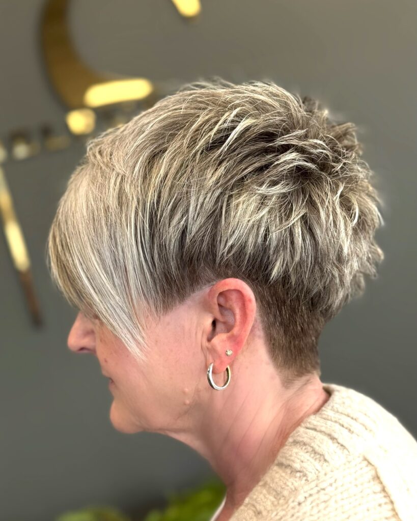 A woman over 60 with a textured multi-tonal blonde and brown shag featuring a buzzed undercut around the ear.