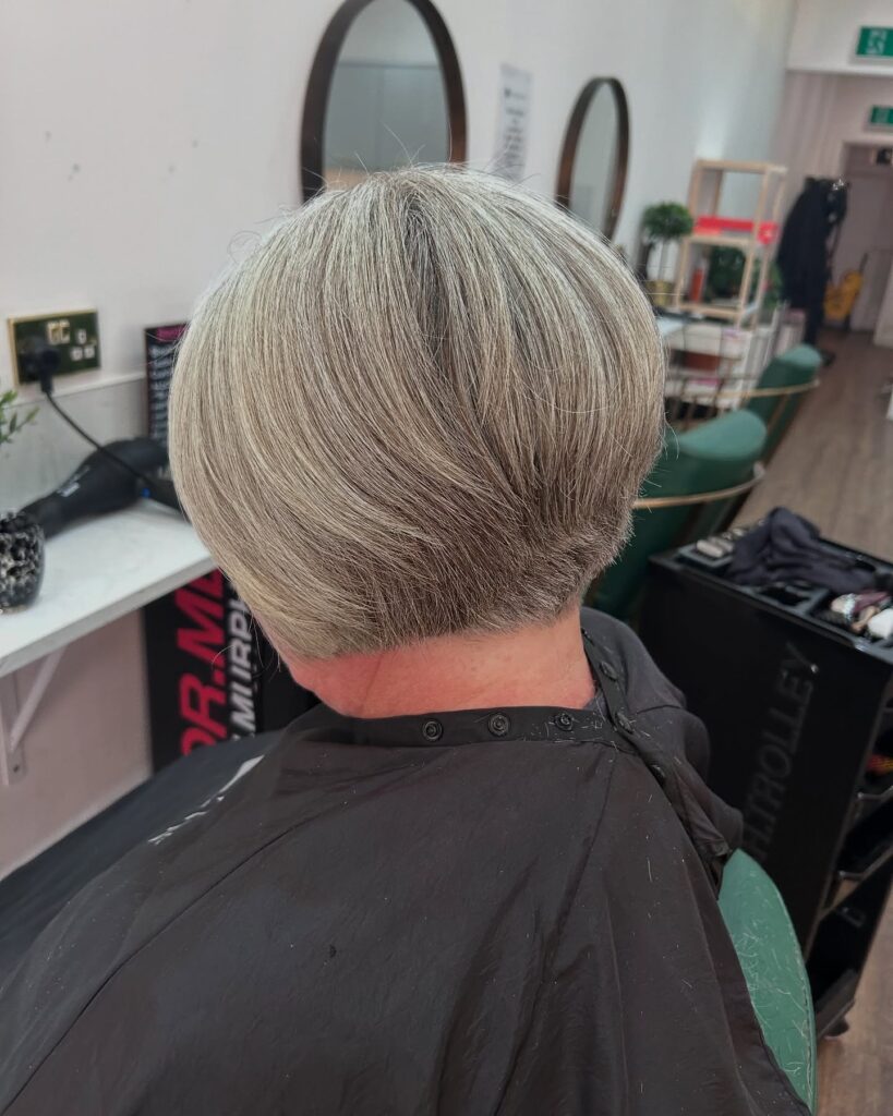 A view from the back of a woman over 60 with a smooth salt-and-pepper bob and a short buzzed nape undercut.
