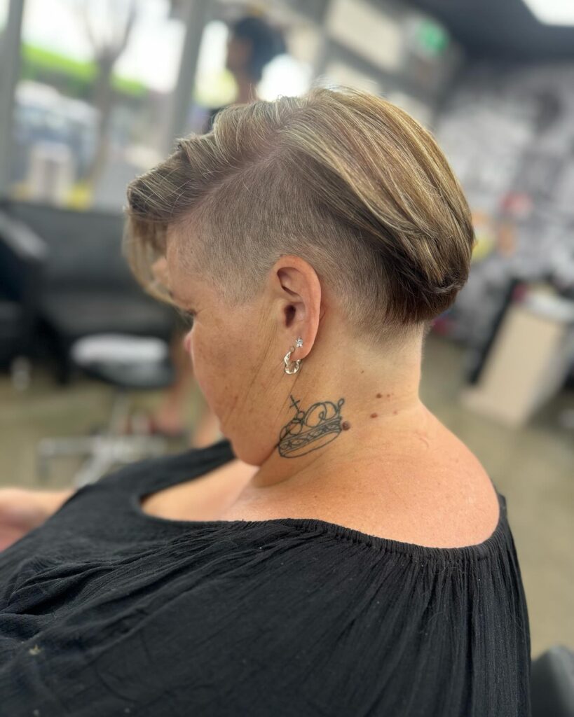 A woman in profile with a sandy blonde pompadour hairstyle featuring a long swept-back top and a high shaved undercut on the side and back.