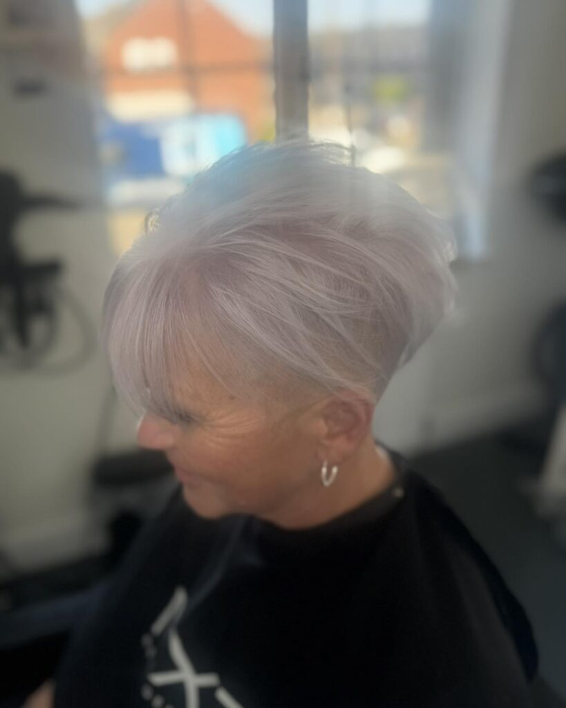 A woman with short, icy white hair in a textured pixie cut with long wisps on top and a shaved undercut visible on the side.